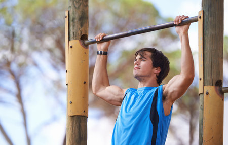 Determination is everything. Young adult male using outdoor gym apparatus.