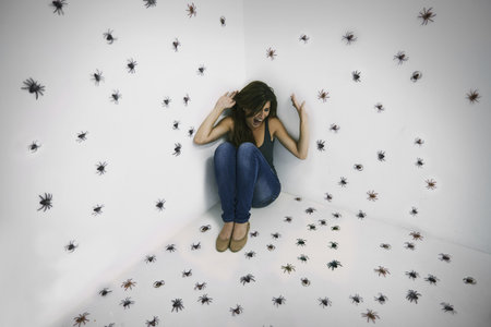 Arachnophobics worst nightmare come true. A young woman crouched in terror while surrounded by spiders.の写真素材