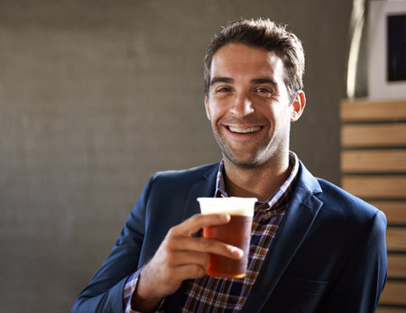 Ice cold brews are the best. Portrait of a handsome young man enjoying an ale at the bar.の写真素材