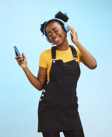 Black woman, phone and music in studio with smile, happiness or listening by blue background. Happy...