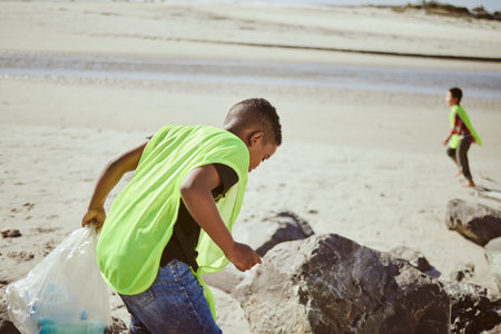 Environment, cleaning and children with plastic on beach for clean up, pollution and eco friendly volunteer. Sustainability, recycle and boy reduce waste, trash and global warming on beach sandの写真素材