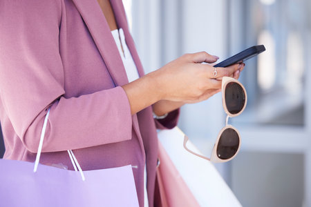Woman, phone and shopping with sunglasses in hands while doing online shopping, ecommerce and internet banking. Female using mobile app for customer discount or coupon on commerce website at a mallの写真素材