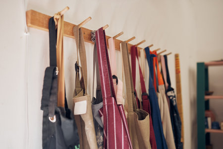 Clothing rack, apron and workshop of clothes hanging on a creative studio wall for art, style or design. Closeup of aprons or work equipment for artistic development on rack for business startupの写真素材