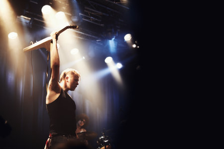 Rocking out. A guitarist on stage with his band beneath strobe lights in a nightclub.の写真素材