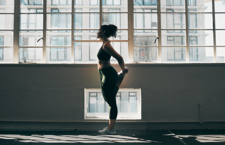Exercise, stretching and a woman at gym for fitness workout for health and body wellness with muscle warm up. Sports female or athlete stretch legs at window for balance, energy and healthy lifestyleの写真素材