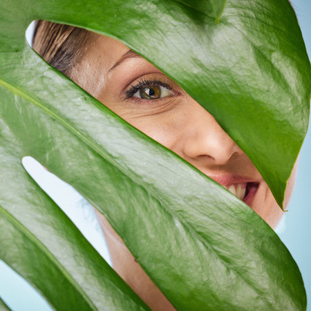 Portrait, skincare and palm leaf with a model woman posing in studio on blue background for beauty....