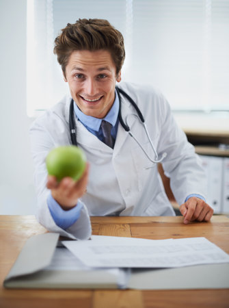 The easiest way to better health. Portrait of a positive young doctor holding up an apple and smiling at the camera.の写真素材