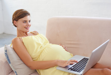 Sharing this special time online. a beautiful pregnant woman relaxing on the sofa at home with a laptop.の写真素材