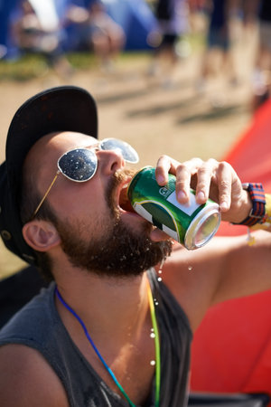 Enjoying a frosty one on a hot day. a guy drinking beer at an outdoor music festival.の写真素材