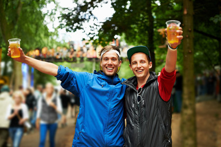 Cheers to us. two friends drinking beer and having a good time at an outdoor music festival.の写真素材