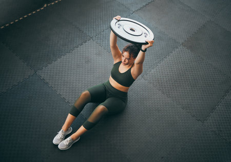Fitness, weight plate and woman at gym for workout, exercise and training for health and body wellness. Top view of strong sports female or bodybuilder on floor weightlifting for power and balanceの写真素材