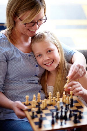 Learning the game. A young blonde girl playing chess with her mother.