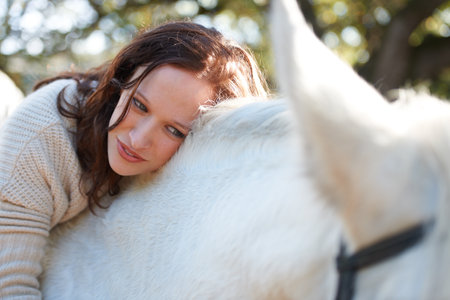 The special bond between horse and rider. An attractive woman looking at and sitting on her horse.の写真素材