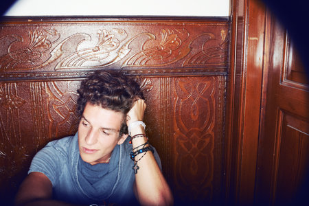 Feeling the loneliness. A young man sitting in a hallway resting his head on his arm and looking...