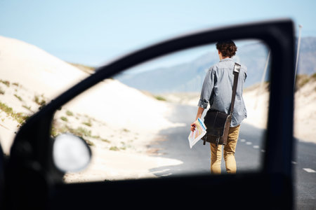 Exploring the countryside. Rear-view of a young man walking down the road holding a map, framed by a car door window in the foreground.の写真素材