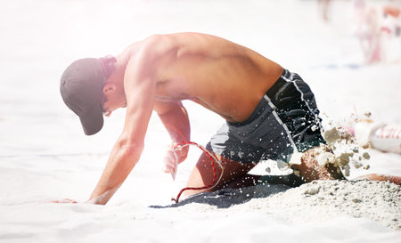 Setting up at the beach. A young man digging in the sand at the beach.