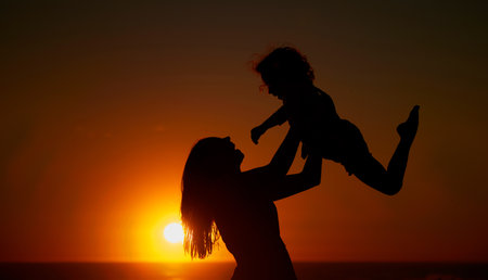 Happy mother and her adorable little girl having fun on the beach. Mom lifting little girl while enjoying family time by the beachの写真素材