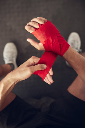 mma boxer wrapping their hand from above. Combat fighter ready for training workout. Athletic fighter prepare for boxing workout. Boxer wrapping bandage on their hand in the gymの写真素材