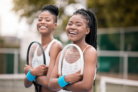 Portrait of cheerful tennis players holding rackets. Young friends ready for tennis practice on the court. African american tennis players laughing and bonding on the courtの写真素材