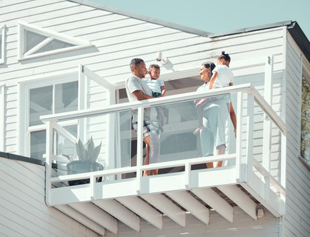 Happy mixed race family with two children wearing pyjamas while standing on balcony at their new house or while on holiday. Young parents talking while holding their son and daughter outsideの写真素材