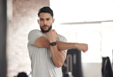 Portrait of one fit young hispanic man stretching arms and shoulders for warmup to prevent injury...