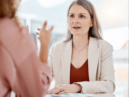 Two happy caucasian businesswomen having a meeting at a table in an office at work. Female businesspeople going through a document and choosing between colour swatches together while talking at workの写真素材