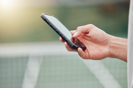 Closeup of unknown mixed race tennis player using cellphone during break in game on court. Hispanic fit athlete browsing internet and networking on phone after match. Active healthy man in sports cluの写真素材