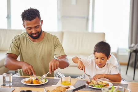 Closeup of a mixed race male and his son enjoying some food at the a table during lunch at home in the lounge. Hispanic father smiling and eating alongside his son at homeの写真素材
