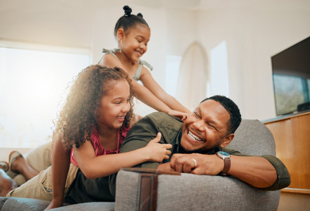 A happy mixed race family of three relaxing in the lounge and being playful together. Loving black single parent bonding with his daughters while playing fun games on the sofa at homeの写真素材