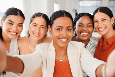 Portrait of a diverse group of five happy businesswomen taking a selfie together at work. Joyful businesspeople taking a photo in an office. Women working in corporate taking a pictureの写真素材