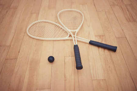 Group of squash equipment and gear on wooden floor in empty court in sports centre with copyspace. Two rackets and ball arranged in sporty arena with nobody before championship game and competitionの写真素材