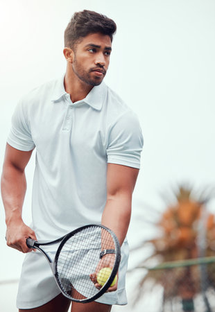 Serious indian tennis player getting ready to serve on court alone. One ethnic fit athlete holding a racket and ball during match. Focused active and healthy man playing game as exercise and trainingの写真素材