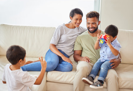 Young mixed race family bonding in the lounge while the parents relax on the couch while their two little sons play. Hispanic couple smiling while watching their boys playing in the living roomの写真素材
