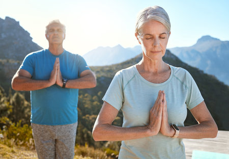 Senior couple meditating with joined hands and closed eyes breathing deeply. Mature couple doing yoga in nature living a healthy and active lifestyle in retirementの写真素材