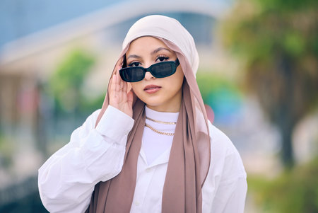 Beautiful young arab woman posing outdoors in a headscarf. Attractive female muslim wearing a hijab posing outside. Shes all about style and fashion. Mixed race woman looking confident and trendyの写真素材