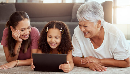 Adorable little mixed race child bonding with single mother and grandmother and using digital tablet...