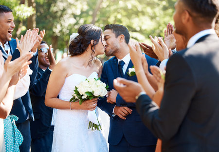 Bride and groom kissing after wedding ceremony while friends and family clap and celebrate their wedding dayの写真素材