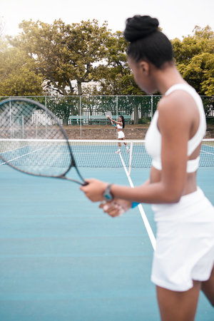 Young woman serving during a tennis match. Two women playing a game of tennis together. African american athletes enjoying a practice match of tennis. Women standing on the courtの写真素材