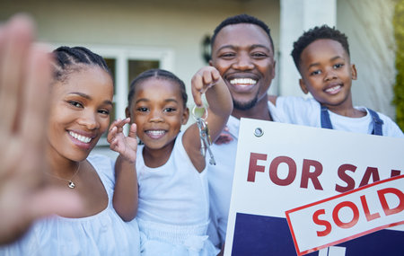 We bought the house. a young family posing in front of a house with a sold sign.の写真素材