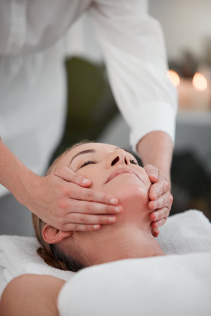 Keeping her skin youthful. a woman receiving a facial massage while at a spa.の写真素材