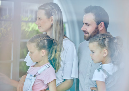 The weather looks great today. a young family looking out of their window from their lounge at home.