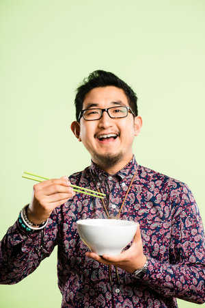 Can you eat with chopsticks. a handsome young man sitting alone in the studio and eating with chopsticks.の写真素材