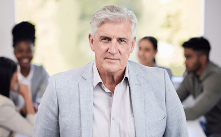 A person who is quietly confident makes the best leader. Portrait of a senior businessman standing in an office with his colleagues in the background.の写真素材