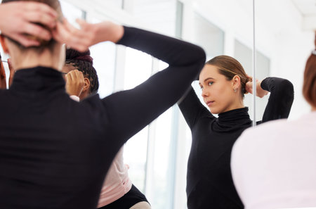 There will be no loose hairs. a young ballerina doing her hair before rehearsal.