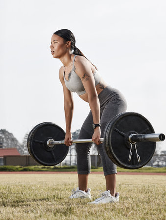Be the best version of you. a young woman using a barbell while exercising outdoors.の写真素材