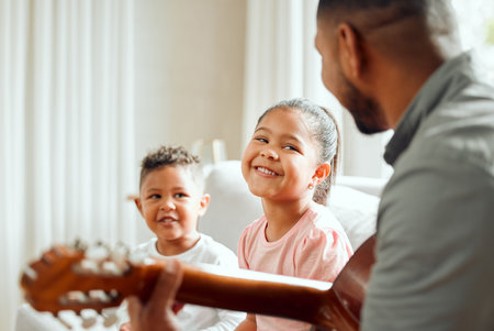 Our talented daddy. a young father teaching his kids how to play the guitar while sitting on the sofa at home.の写真素材