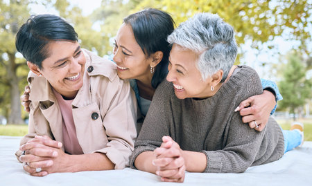 Love, family and lesbian couple with adult daughter, happy and laughing, relax and talking in a park. Lgbt, happy family and woman enjoying a picnic with her mothers, cheerful and excited while lyingの写真素材