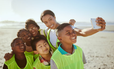 People, phone and selfie for eco friendly environment with smile at the beach for recycling in nature. Happy woman with kids smiling for photo by the sandy ocean looking at smartphone with vestsの写真素材