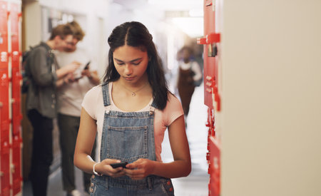 Staying in school is the smart thing to do. a teenage girl using a smartphone next to her locker at high school.の写真素材