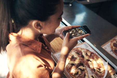 Todays lunch deserves a shoutout. an unrecognizable woman standing alone and using her cellphone to photograph her pizza at a restaurant.の写真素材